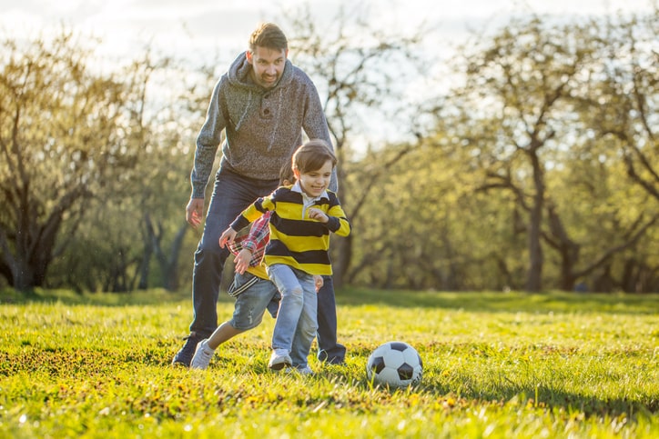 Dad and two kids play soccer outside. Work-life balance image. Report card advice for parents. 