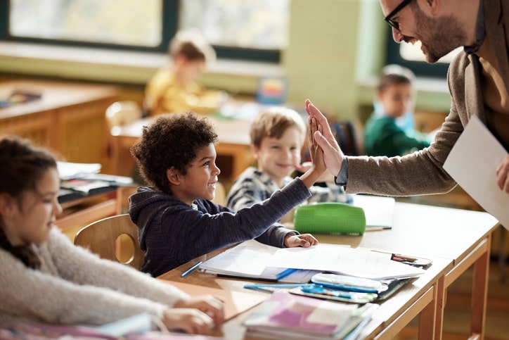 Teacher high-fives young student. Report card advice for parents: every child is different. 